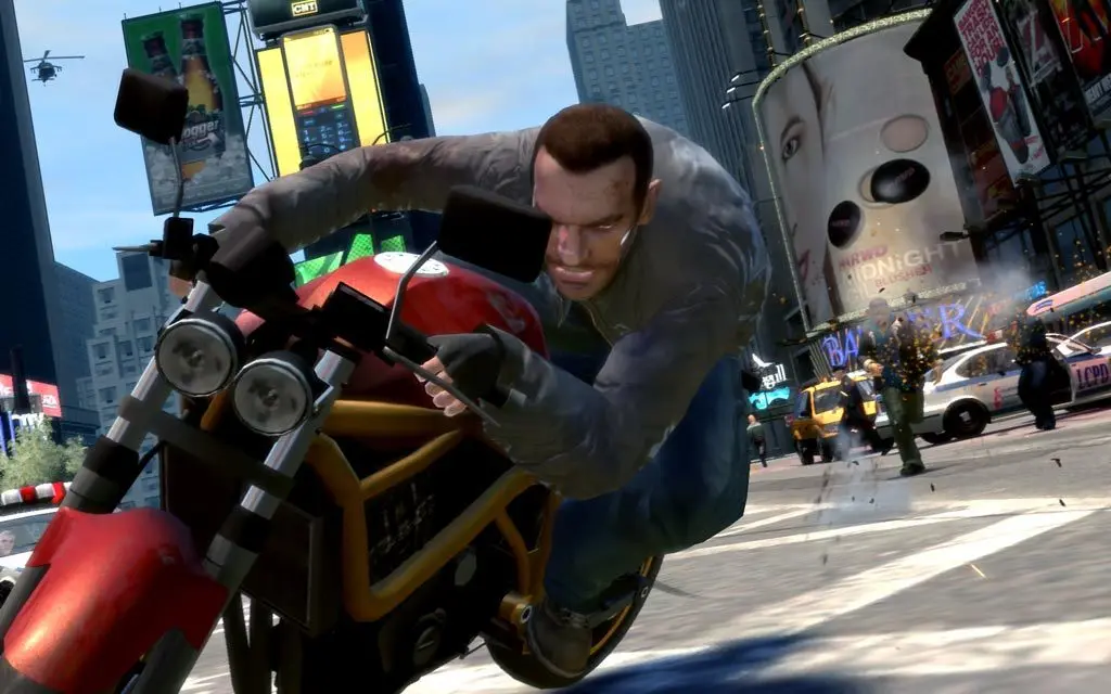 Niko Bellic leaning hard into a red sport bike at full speed through Star Junction, Liberty City's neon-lit intersection, a helicopter in the sky and police cars on the right