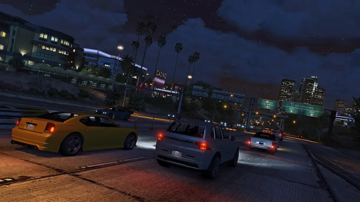 A Los Santos street at night in GTA 5, red taillights of passing cars, lit-up skyscrapers in the distance, an urban chase atmosphere