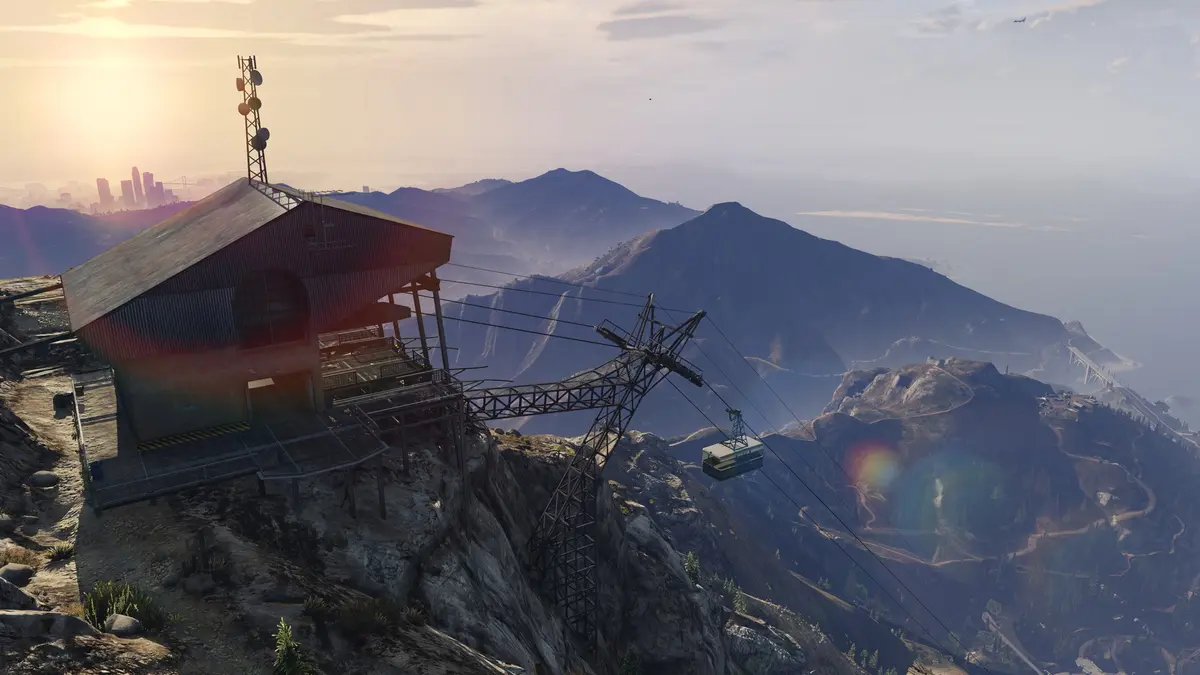 GTA 5 screenshot: the cable car station at the top of Mount Chiliad at sunrise, with a panoramic view of the mountains, the ocean and the distant Los Santos skyline