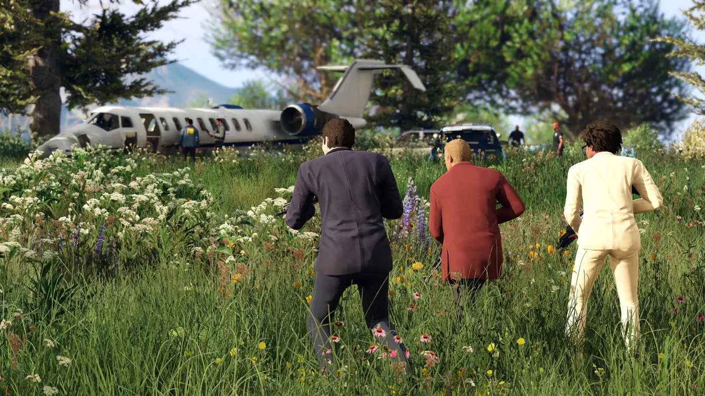 GTA V screenshot: three men in suits, one dark, one burgundy and one cream, advance armed through tall flowering grass toward a crashed private jet surrounded by agents and vehicles