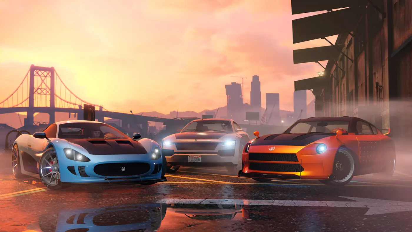 Official GTA Online screenshot: three sports cars, a blue supercar, a white sedan with its headlights on, and an orange tuned coupe, lined up on a wet road at sunset, with a bridge and the Los Santos skyline in the background
