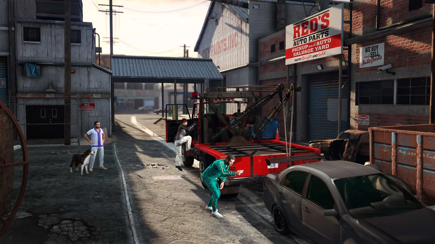 The storefront of Red's Auto Parts in GTA Online, a scrapyard in an industrial district of Los Santos at sunset, a red tow truck parked in front of the sign, two characters in tracksuits and a dog on the road