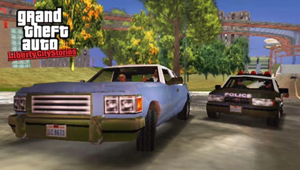 Light blue sedan chased by a police car on a tree-lined road in Liberty City, with the elevated train in the background