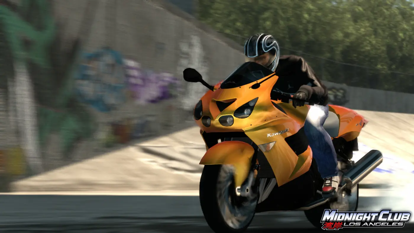 A rider in a black helmet leaning over an orange Kawasaki superbike, flying at full speed along a graffiti-covered wall in Midnight Club: Los Angeles, with a heavy motion-blur effect.
