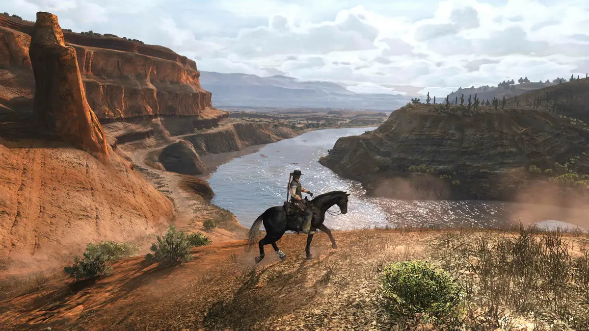 A rider on a black horse follows the edge of a red rock canyon above a river, under a cloudy sky