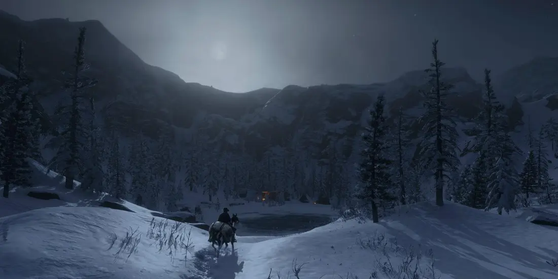 Lone rider riding through a snowy mountain landscape at night, under a veiled moon, toward a frozen lake lined with pines in Red Dead Redemption 2