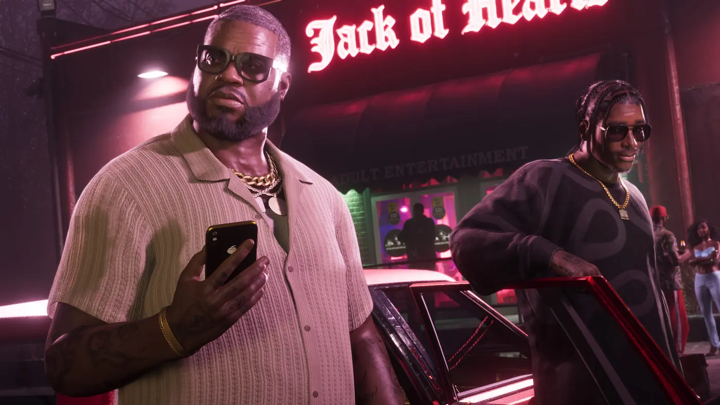 An imposing man in a light shirt and a heavy gold chain holds a smartphone in front of the red neon Jack of Hearts sign of an adult club at night in GTA VI, a second character with braids near a classic car with a red hood